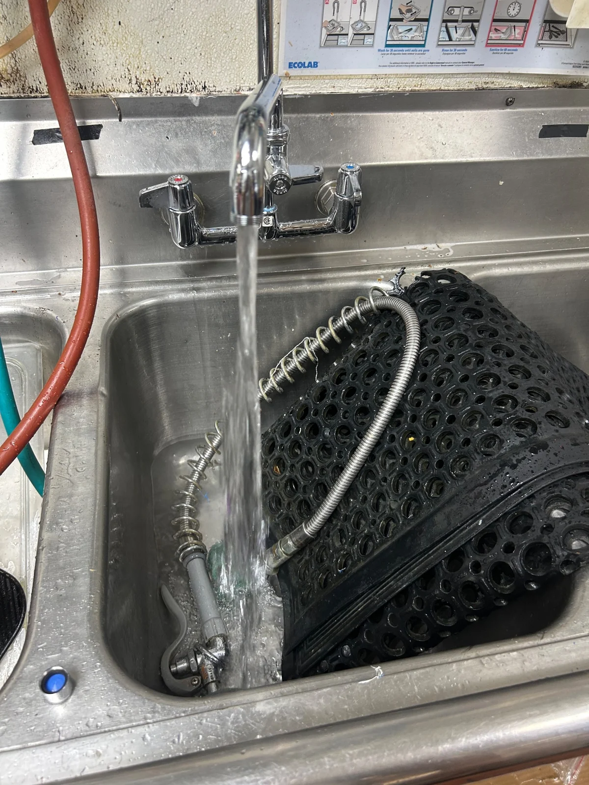 Water flowing from a chrome faucet into a stainless-steel kitchen sink, with a sprayer hose in the basin.