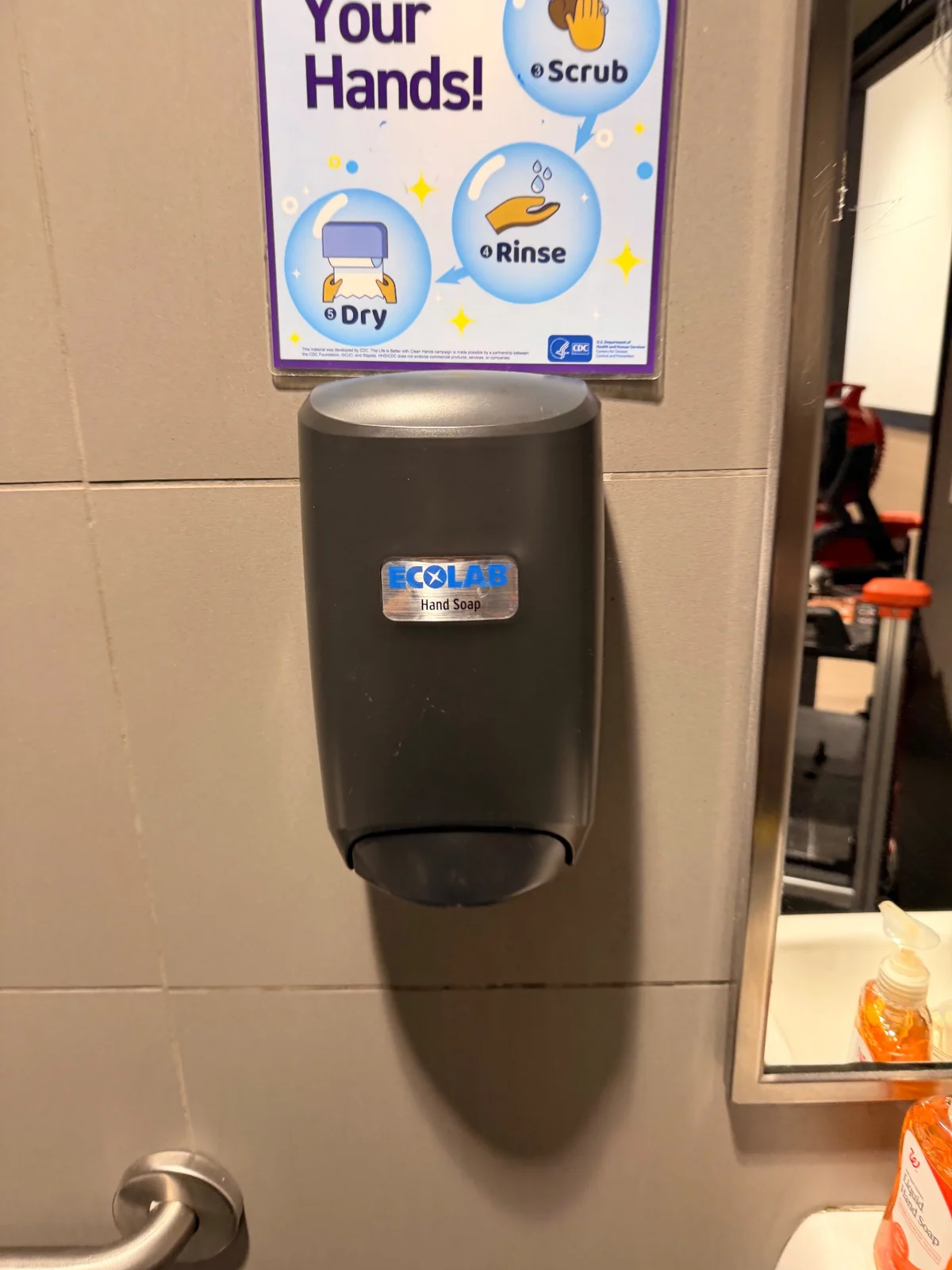 A closed soap dispenser mounted on a tiled restroom wall.